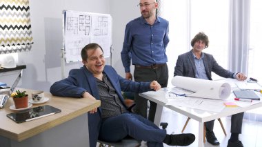 Bir grup mutlu girişimci başarılı bir anlaşma yaptıktan sonra konferans odasında gülümseyip kahkaha atıyorlar. Üç adam planlar ve inşaat planlarını tartışıyor.