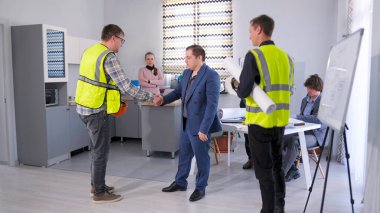 Bir grup insan konferans odasında el sıkışıyor. Ustabaşı müşteriyle el sıkışıyor. Tahminlerin ve proje detaylarının tartışılması. Mimarlık bürosunun çalışma günleri..