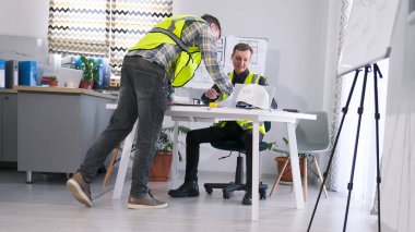 Yeşil sinyal yelekli iki adam bir inşaat şirketinin ofisinde bir projeyi tartışıyorlar. Ustabaşı ve müteahhit proje tahmini üzerinde hemfikir. Takım çalışması.