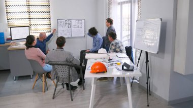 Bir grup iş adamı bir masada oturuyor, önlerinde çizimler ve planlarla dolu beyaz bir tahta var. İnşaat fikirlerini tartışıyorlar. Mühendisler ve mimarlar mini bir sunumda. Bilgilendirme