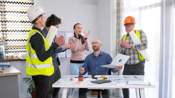 İnşaat şirketi çalışanları patronlarını alkışlıyor. Bir grup inşaatçı, mühendis ve tasarımcı iyi bir iş çıkardılar. Masanın etrafında dizüstü bilgisayarla duruyorlar.