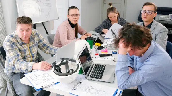 Bir grup mimar dizüstü bilgisayar ve kağıtlarla dolu bir masada oturuyor. Birlikte bir proje üzerinde çalışıyorlar. Takım çalışması ve takım oluşturma. Mimarlık bürosunun çalışma günleri..