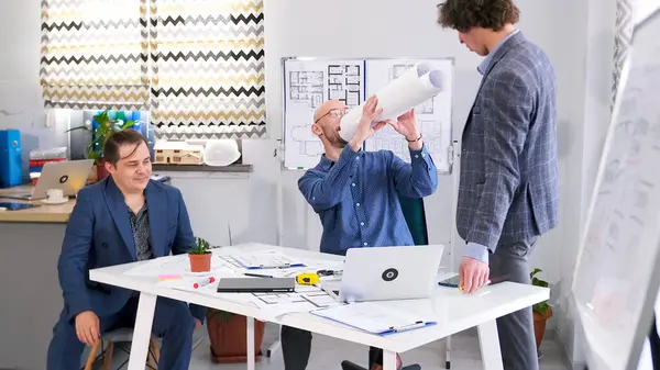 Mimarlık bürosunun çalışanları ofiste oyalanıyorlar. Üç adam bir proje üzerinde çalışıyor. Mühendisler proje için tahminlerde bulunuyor. Bir grup insan konferans odasında bir masada oturuyor.