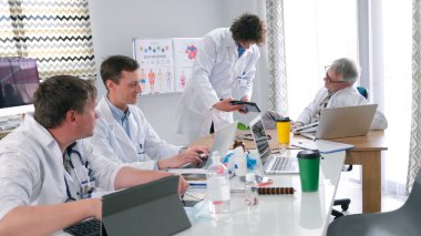 Genç bir stajyer, hastanın testlerini başhekime getirir. Beyaz önlüklü bir grup adam dizüstü bilgisayarlı bir masada oturuyor ve hasta için bir tedavi sistemi geliştiriyor.