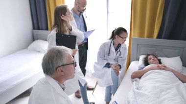 Gri saçlı yaşlı bir doktor ve bir grup stajyer bir hastanın tedavi planını tartışıyorlar. Bir grup doktor hasta bir öğrencinin yattığı yatağın etrafında duruyor..