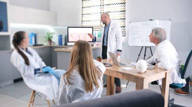 Saç nakli kliniğinden bir grup araştırmacı samimi bir konferans odasında masanın etrafında toplandı. Doktorlardan biri bilgisayar ekranını işaret ediyor. Meslektaşlarına sunum yapıyor.