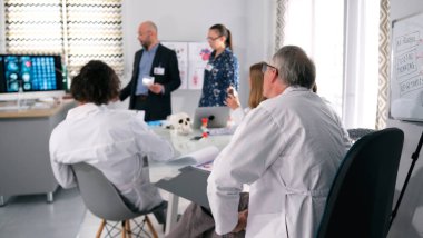 Beyaz laboratuvar önlüklü bir grup insan konferans odasındaki bir masanın etrafında toplandı ve nöroşirürjiyle ilgili bir sunum izliyorlar. İlaç ve sağlık