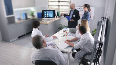 Laboratuvar önlüklü bir grup insan beyin kanseri olan ciddi bir hastanın durumunu tartışıyor. Kliniğin önde gelen doktorları yaklaşan ameliyat hakkında bir sunum yapıyorlar..