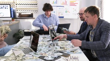 Bir iş adamı ekibi banknotlar ve dizüstü bilgisayarlarla dolu bir masada oturuyor. İnsanlar başarılı bir iş anlaşmasını ya da yatırım fırsatını tartışıyorlar.