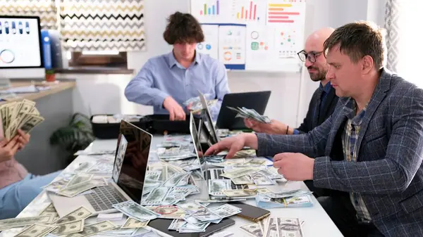 Bir iş adamı ekibi banknotlar ve dizüstü bilgisayarlarla dolu bir masada oturuyor. İnsanlar başarılı bir iş anlaşmasını ya da yatırım fırsatını tartışıyorlar.