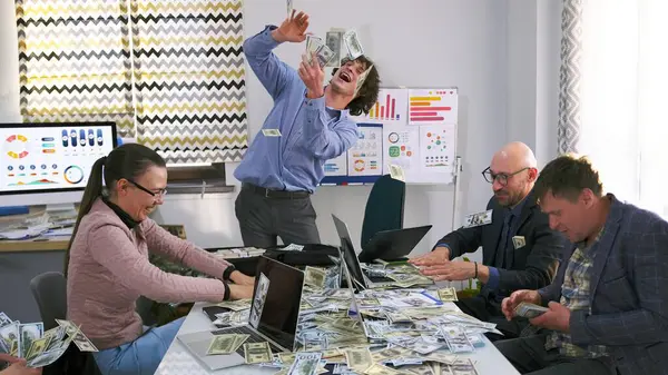 Bir grup ekonomist ve finansör büyük bir anlaşmanın tamamlanmasından memnun. Adam elinde bir tomar para tutuyor, gülüyor, gülümsüyor ve iş arkadaşlarına para saçıyor..