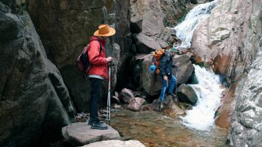 İki erkek yolcu küçük bir şelaleye ulaştı. Yürüyüşçüler kayalıklarda durur ve kanyonun manzarasının tadını çıkarırlar. Aşırılık ve özgürlük. Güzel doğa..