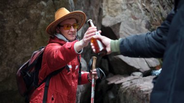 Bir adam dağdaki arkadaşına bir şişe bira uzatıyor. Eşcinsel bir çift doğada eğleniyor. Seyahat ve turizm. Kamp gezisinde alkol.