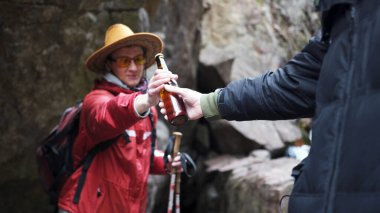 Arkadaşlar dağlarda bira içer. Kırmızı ceketli bir adam bir bira tutuyor ve başka bir adama uzatıyor. Rahatlama ve sükunet. Yürüyüş ve maceralar.
