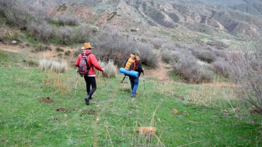 İki kardeş sırt çantalarıyla bir tarlada yürüyorlar ve biri kırmızı ceket ve komik bir kovboy şapkası giyiyor. Çocuklar macera aramak için vahşi doğada yürüyorlar..