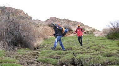 İki arkadaş dağlık bir alanda yürüyorlar. Resim huzurlu ve huzurlu, grup doğanın ve manzaranın güzelliğinin tadını çıkarıyor..