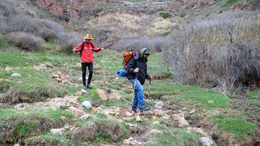 Profesyonel bir rehber, genç bir adama bilinmeyen bir yol gösteriyor. İki kişi ormanda toprak bir patika boyunca yürüyor kayaları, çalıları ve dağları geçiyor.