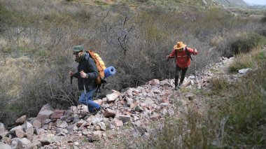 Rehber ve asistanı yeni yerler keşfettiler. Hafta sonu kamp gezisi. Dağlarda gezinti. Sırt çantalı ve yürüyüş direkli iki kişi kayalık tepeye tırmanıyor.