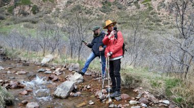 İki gezgin, telefonlarında birkaç fotoğraf çekmek için küçük bir dağ nehrinde durdular. İki adam kayalık bir nehir kıyısında duruyor. Erkekler doğayı sever
