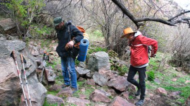Gezginler sırt çantalarını giyip yola koyuldular. İki kişi kayalık bir patika boyunca ormanda yürüyorlar. Macera ve kamp. Gezinti ve yürüyüş.