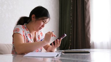 Ciddi, odaklanmış bir kadın koridorda büyük bir masada oturuyor. Asyalı bir iş kadını elinde cep telefonuyla bir masada oturuyor. Defter ve tablet masanın üstünde..