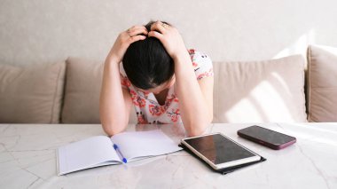 Endişeli bir kadın elinde defter, telefon ve tabletle masada oturuyor. Depresyon, acı, başarısızlık. Yorgun kadın başını eğmiş, hiçbir şey yapamıyor.