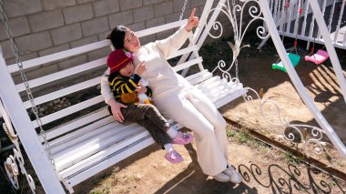 Bir bebek bakıcısı salıncakta bir çocukla oturur. Şefkatli bir anne küçük kızıyla tatlı tatlı konuşur. Bir kadın ve bir bebek evin bahçesinde salıncakta sallanıyorlar.