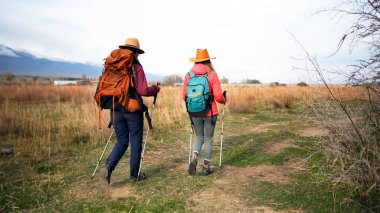 Sırt çantalı iki kız öğrenci yürüyüşe çıkıyor. Aktif yürüyüşçüler maceralara doğru toprak patika boyunca yürürler. Fitness ve yürüyüş. Doğanın tadını çıkarıyor.