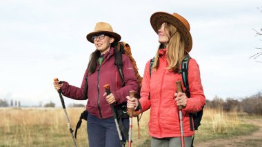 Şapkalı ve sırt çantalı iki mutlu kadın sahada yürüyorlar. Gezginler birlikte seyahat eder. Açık hava fitness. Doğayla birlik. İki lezbiyen arasında bir randevu..