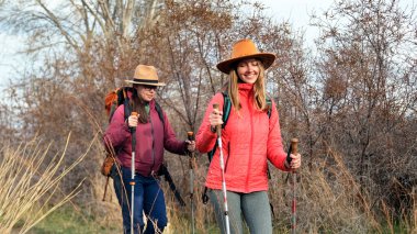 Sırt çantalı ve şapkalı mutlu bayanlar ormanda yürüyor. Genç bir lezbiyen aile yürüyüş yapıyor. Hafta sonu kamp gezisi. Aktif hafta sonları. Yürüyüş ve macera