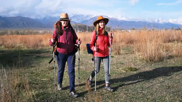 Maceracılık ve macera ruhu. İki güzel genç öğrenci, karlı dağların arka planında çimenli bir arazide geziniyorlar. Kadınlar yürüyüş yapmayı sever.