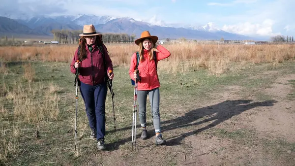 Şapkalı iki lezbiyen kırsalda yürüyorlar. Kadınlar piknik için toplandılar. Sırt çantalı ve yürüyüş direkli kız öğrenciler dağ eteklerinde seyahat ederler.