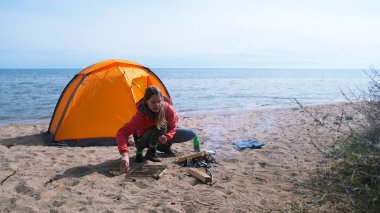 Yalnız ve güzel bir kadın sahilde çadırın yanında oturuyor ve şenlik ateşi yakıyor. Sahne huzurlu ve sakin, arka planda dalgaların sesi var..