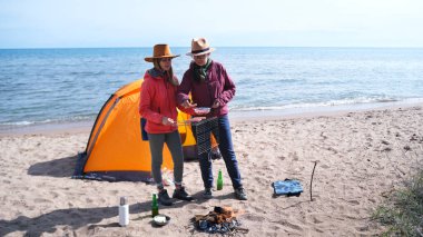 İki güzel genç kadın sahilde bir çadırın yanında duruyorlar. Kamp ateşi yaktılar ve ızgara sosis yapacaklar. Göl kenarında piknik. Uzun zamandır beklenen bir hafta sonu.