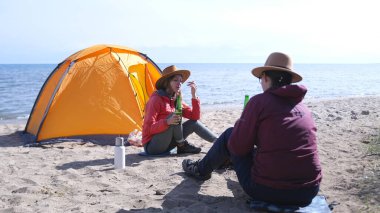 İki genç öğrenci sahilde oturuyor ve bira içiyorlar. Arkalarında bir çadır var. Kadınlar gölün kıyısında dinlenir. Tatiller ve deniz.