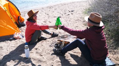 İki kadın sahilde oturmuş yeşil bira şişelerini tıkırdatıyor. Deniz kenarında uzun zamandır beklenen bir tatil. Gezginler çadırı olan yabaniler gibi dinleniyor. Öğrenciler hafta sonlarını aktif olarak geçirirler