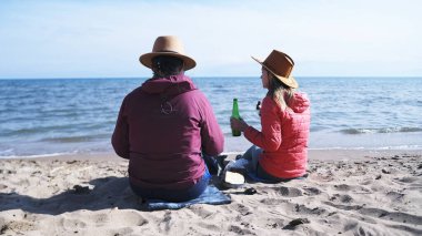 Yorucu bir günün ardından dinlen. İki kişi ellerinde birayla sahilde oturuyorlar. Kadınlar birbirlerine eşlik etmekten hoşlanırlar. Sahne sakin ve aceleci değil.
