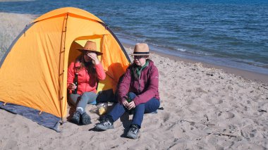 İki kız sahilde çadırın yanında oturmuş bira içiyorlar. En iyi arkadaşlar göl kenarında birlikte eğlenirler. Rahatlama, özgürlük ve seyahat.