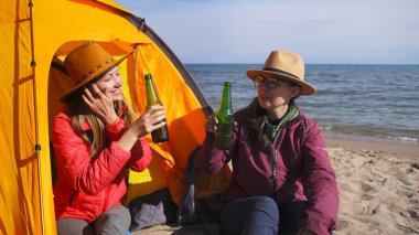 Birbirine aşık iki mutlu kadın sahilde oturmuş ellerinde bira şişeleriyle rahatlıyorlar. Genç kız öğrenciler gülümsüyor ve nehir kenarında dinlenirken eğleniyorlar.