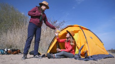 Bir kadın diğerine cips uzatıyor. En iyi iki arkadaş dışarıda bira içip abur cubur yiyorlar. Turistler bir çadırla sahilde dinlenirler. Eylem doğada gerçekleşir.
