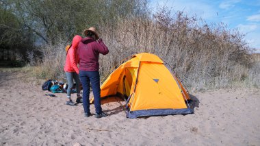 İki kişi sahilde bir çadırın yanında duruyor. Turizm, macera ve seyahat. İki kız kardeş dünyanın genişliğinde birlikte dolaşır. Gezginler bir çadırla plajda dinlenirler..