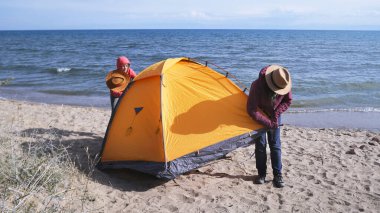 İki kadın sahilde çadır kurdu. Turistler deniz kenarında bir kamp yeri buldular. İki gezgin çadırı tamir ediyor. Macera, yürüyüş ve özgürlük.