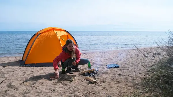 Yalnız ve güzel bir kadın sahilde çadırın yanında oturuyor ve şenlik ateşi yakıyor. Sahne huzurlu ve sakin, arka planda dalgaların sesi var..