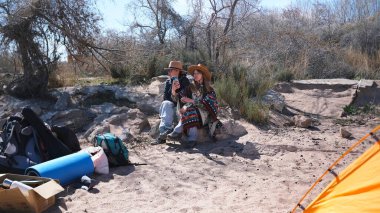 İki güzel kumsalda oturuyor. Yakınlarda bir çadır, sırt çantaları ve diğer turistik eşyalar var. Kadınlar piknik yapmak için deniz kenarına geldiler.