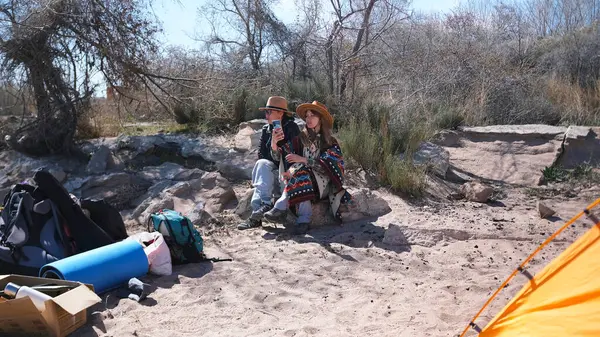 İki güzel kumsalda oturuyor. Yakınlarda bir çadır, sırt çantaları ve diğer turistik eşyalar var. Kadınlar piknik yapmak için deniz kenarına geldiler.