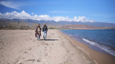 Kırgızistan dağlarında deniz kıyısında iki kız arkadaş geziniyor. Mavi göl manzaralı sahil boyunca yürüyen iki kişi var. Issyk Kul.