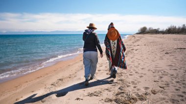 Kumsalda yürüyen, arkadan manzaralı, aşık turistler. Gezginler mavi gölün kıyısında geziniyorlar. İki kız öğrenci eğleniyor. Turizm
