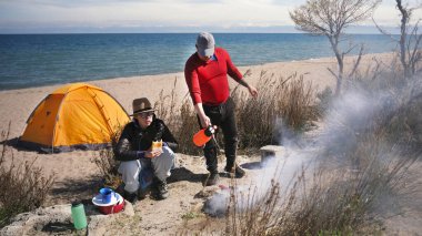 Bir adam ve genç bir kadın sahilde oturmuş et kızartmak için şenlik ateşi yakıyorlar. İki kişi göl kenarında vakit geçiriyor. Arkalarında bir çadır var. Tatiller