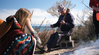 Bir adam eski bir Asya enstrümanı olan Komuz 'u çalıyor. Yanında bir kadın oturuyor, dikkatle ona bakıyor. Yakınlarda bir kamp ateşi tütüyor. Ayin şarkıları. Arkadaşlar rahatlayın