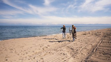 Kamp ateşi için kuru dallar ve yakacak odun arayın. İki kız öğrenci sahilde yürüyor ve çöpleri topluyorlar. İki kişi deniz kıyısında geziniyor.